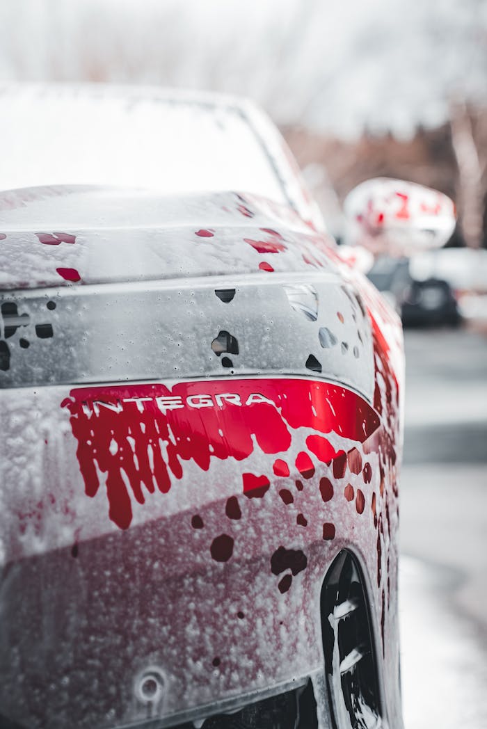 services-03 Close-up of a red Integra car being washed, showcasing water droplets and soap.