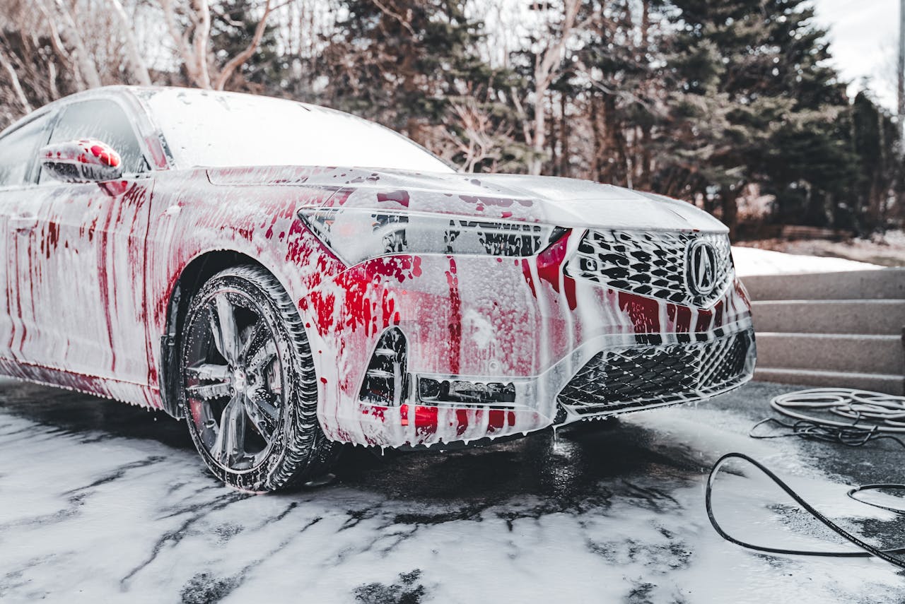 heros-img A vibrant red car covered in soapy foam during a thorough outdoor wash under daylight.
