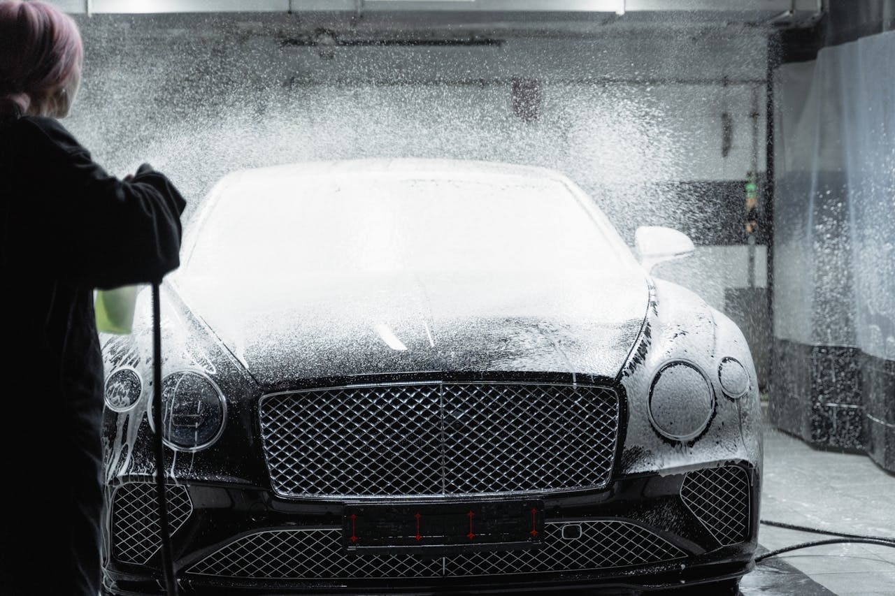 services-01 Black luxury car receiving a foamy wash in an indoor car wash service.